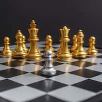 Lohnt es sich, jetzt zu investieren? Auf einem Schachbrett steht eine Grosszahl goldiger Schachfiguren einer einzelnen Figur in silberner Farbe entgegen.