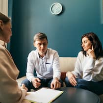 Gelten frühere Vereinbarungen auch weiterhin? Ein junges Paar sitzt in einem Büroraum zusammen mit einer Beraterin. Die Frau wirft dem Mann einen kühlen Blick zu. Ist ein Scheidungsverfahren hängig, fallen gegenseitige Begünstigungen aus Testament oder Erbvertrag von Gesetzes wegen dahin.