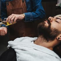 Schädliche Substanzen in Bartpflegeprodukten – die Hersteller reagieren Ein Kunde liegt auf einem Friseurstuhl in einem Barbershop und lässt sich seinen Bart mit einem kosmetischen Öl behandeln. Genau in solchen Bartpflegeprodukten wurden Inhaltsstoffe gefunden, die Allergien auslösen können und teils gar verboten sind.