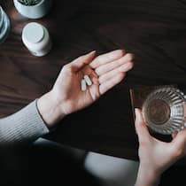 Was gegen Antidepressiva spricht – und was dafür Eine Frau hält in ihrer offenen Handfläche zwei Tabletten und in der anderen ein Glas Wasser. Was gegen Antidepressiva spricht – und was dafür