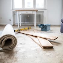 Lieber Handwerker, kommst du endlich? Unfertige Handwerksarbeiten liegen in einem Wohnzimmer herum, welches mit einem Teppich neu verlegt werden soll. Bei Lieferverzug von Handwerkern ist es wichtig, nicht zu spät zu reagieren. So gehen Konsumentinnen und Konsumenten vor.