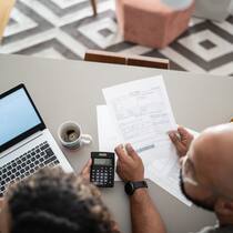 Bis wann eine Korrektur fordern? Ein Paar kontrolliert eine Rechnung mithilfe eines Taschenrechners und einem Laptop, der auf dem Küchentisch liegt.
