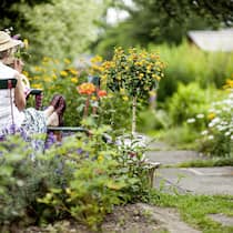 So sorgen Sie dafür, dass der Garten zu Ihnen passt Deutschland, Tee trinkende Seniorin sitzt am Tisch in einem sommerlichen Garten.