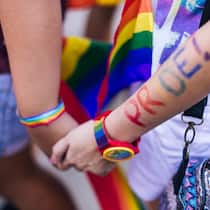 Was bedeutet LGBTQIA+? Ein Pärchen an einer Demonstration für die Rechte der LGBT-Community hält sich die Hände, im Hintergrund ist eine Regenbogenflagge zu erkennen. Wofür steht die Abkürzung «LGBTQIA+» und was gilt bezüglich dem Diskriminierungsverbot?