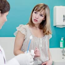Muss das wirklich sein? Eine Ärztin bereitet einen medizinischen Abstrich des Gebärmutterhalses vor, während die Patientin daneben sitzt und sich bezüglich der Behandlung erkundigt.