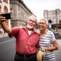 So haben Sie im Alter genug Geld Ein pensioniertes Paar in den Ferien macht ein Selfie auf einer breiten Strasse.