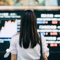 Soll ich jetzt die Fonds anpassen? Eine junge Frau steht vor einem Display, welches die aktuellen Trends an der Börse anzeigt.