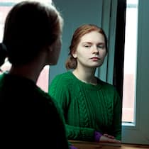 Wieso wir uns selber schlecht einschätzen können Eine junge Frau schaut sich im Spiegel an.