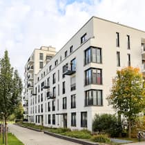 Welche braucht es? Moderne Wohnungen einer Stockwerkeigentümergemeinschaft mit Zugang über einen Gehweg umgeben von Bäumen.