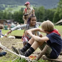 «Wir treffen den Zeitgeist» Zwei Pfadfinder und eine Pfadfinderin sitzen auf einer Wiese, reden und lachen