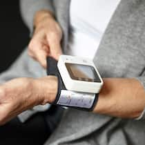 Welche Blutdruckmessgeräte zuverlässig sind Eine Frau befestigt ein Blutdruckmessgerät am Handgelenk.