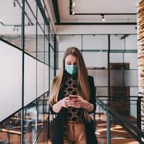 Darf ich trotz Verbot ins Büro? Eine Angestellte mit Schutzmaske geht durch ein Grossraumbüro und tippt gleichzeitig auf ihr Smartphone.