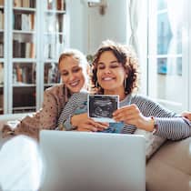 Einmal Einstein, bitte schön? Ein lesbisches Paar freut sich über die Schwangerschaft und hält ein Ultraschallfoto in eine Laptopkamera.