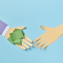 Freunden Geld pumpen: Darauf sollten Sie achten Eine Hand aus Papier gefaltet, überreicht einer zweiten Papierhand ein kleines Bündel mit Post-its, das sinnbildlich für Geld steht - Wer anderen ein Darlehen vermacht, sollte dies vertraglich festhalten, um die Rückzahlung des Privatdarlehens durch den Schuldner zu regeln.