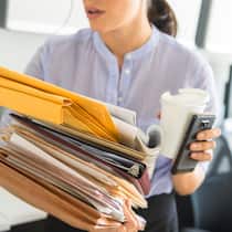 Keine Angestellten zweiter Klasse Eine gestresste Mitarbeiterin schleppt einen Stapel Dokumente in der einen Hand in der anderen einen Kaffeebecher und ein Handy