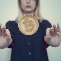 Wie erhalte ich das Geld zurück? Eine Frau balanciert eine Bitcoin-Münze auf einem Faden, den sie ausgestreckt in beiden Händen hält.