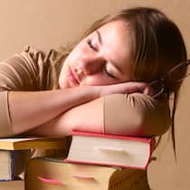 Klüger über Nacht Eine junge Frau schläft, auf einen Stapel Bücher gelehnt.