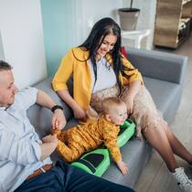 Wer erhält die Familienzulagen? Eine junge Familie sitzt in ihrem Wohnzimmer auf dem Sofa. Zwischen ihnen liegt der kleine Sohn.