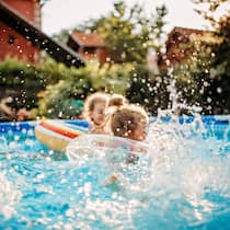 Pool-Party im Gemeinschaftsgarten – ist das erlaubt? Kleine Kinder plantschen vergnügt in einem aufgestellten Pool im Garten einer ruhigen Wohngegend.