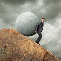 Der Weg ist steinig, aber machbar Ein Geschäftsmann versucht einen grossen kugelförmigen Stein über einen felsigen Gipfel zu stossen.