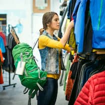 Naturfreunde im Plastik-Dilemma Eine junge Frau stöbert in einem Outdoor-Geschäft nach Windjacken und trägt einen Wanderrucksack, den sie sich bereits ausgesucht hat.