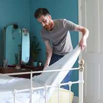 Wenn die Mitbewohner zum Problem werden Ein Mann schüttelt seine Bettdecke aus und richtet das Bett wieder her.