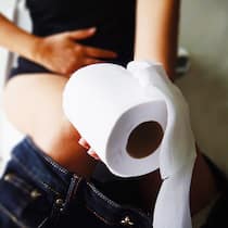 Was tun bei Blut im Stuhl? Eine Frau sitzt auf der Toilette und hält sich den Bauch.