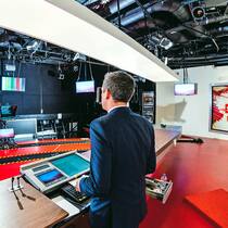 Was dürfen Fernseh- und Radiosender? Ein Tagesschau-Moderator von SRF ist von hinten zu sehen. Er blickt auf diverse Bildschirme im Fernsehstudio.