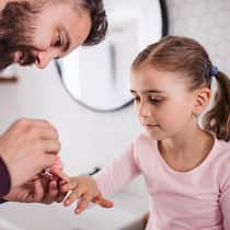 Wer zahlt wie viel bei alternierender Obhut? Ein kleines Mädchen hat ihre rechte Hand ausgestreckt, damit ihr Vater die Nägel lackieren kann.