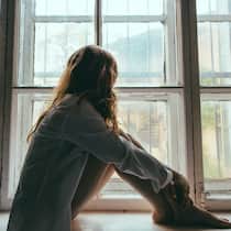 «Ich fühle mich zunehmend einsam» Eine junge Frau sitzt zusammengekauert am Fenstersims ihrer Wohnung und hat ihren Blick auf die umstehenden Häuser der Nachbarschaft gerichtet.