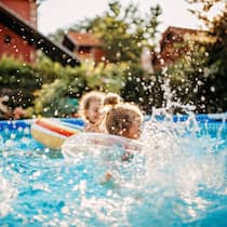 So geht Ihre Pool-Party nicht baden Kleine Kinder plantschen vergnügt in einem aufgestellten Pool im Garten einer ruhigen Wohngegend.