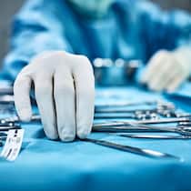 Schmerzen nach der Operation – was tun? Chirurg greift nach chirurgischen Instrumenten