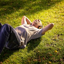 Der Soundtrack der Einsamkeit Mann liegt auf Wiese und hört Musik mit Kopfhörern