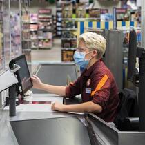 Nicht mehr kranke Mitarbeitende als sonst Kundin mit Schutzmase bezahlt an der Migros-Kasse
