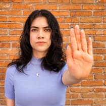 Sie sind nicht machtlos gegen häusliche Gewalt Eine junge Frau steht vor einer Mauer und streckt ihre Hand aus, mit der Handfläche Richtung Kamera.
