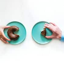 So holen sich Frauen mehr Zwei verschiedene Hände greifen nach zwei unterschiedlich grossen Donuts. Die Hand der Frau hat ein grösseres Donutstück als die Hand des Mannes.