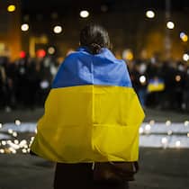 Der Beobachter hilft Eine Frau trägt eine ukrainische Flagge und spricht vor einem Meer aus Kerzen und den versammelten Demonstranten ihre Solidarität mit den Ukrainerinnen und Ukrainern aus, die vom russischen Angriffskrieg betroffen sind.