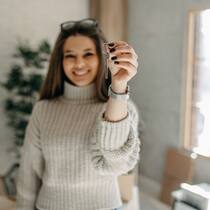 Was muss ein Nachmieter erfüllen? Eine Mieterin steht in einer Wohnung, in die sie gerade eingezogen ist, und hält erfreut einen Wohnungsschlüssel in der linken Hand.