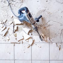 Was tun, wenn der Vermieter sanieren will? Ein blauer Presslufthammer liegt auf zerstörten Badezimmerkacheln.