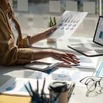 Da muss eine professionelle Verwaltung ran Eine Frau sitzt an einem Bürotisch, auf dem Laptop sowie zahlreiche auf Papier ausgedruckte Diagramme liegen. Beim Stockwerkeigentum kann eine Verwalterin das Leben der Eigentümer um einiges einfacher machen. Jedoch kostet dieser Service, weshalb man die Wahl einer Verwaltung nicht leichtsinnig treffen sollte.