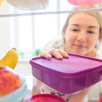 Tipps zum Stromsparen in der Küche Eine junge Frau stellt ein Tupperware in den Kühlschrank.