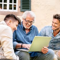 Soll ich Rechnungen mit E-Bill bezahlen? Ein Vater sitzt mit seinen beiden erwachsenen Söhnen im Garten seines Hauses und hat einen Laptop bei sich.