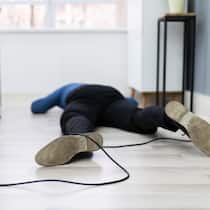 Gilt das als Berufs- oder Freizeitunfall? Ein Angestellter im Homeoffice liegt auf dem Fussboden, weil er über ein Kabel am Boden gestolpert ist.