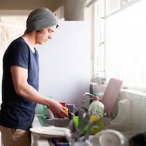 Teure Wohnung – wie viel zahlt der Staat? Ein junger Mann steht in der Küche und wäscht Geschirr ab. Günstiger Wohnraum ist für Sozialhilfebeziehende oft schwer zu finden.