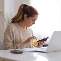 Wie Sie Fehler im Vorsorgeausweis entdecken Eine Frau sitzt vor einem Laptop und tippt auf einem Taschenrechner - Wissen Sie, wie es um Ihre 2. Säule steht? Sie sehen das im jährlichen Vorsorgeausweis Ihrer Pensionskasse. Der Beobachter zeigt, wie Sie die Zahlen prüfen können – es lohnt sich!