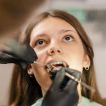 Prämie für Tochter (10) mehr als verdoppelt – Familie in der Falle Teenage girl at dentist office sitting on chair while doctor checking and setting her dental braces.