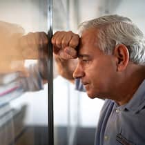 Ist das Pensionskassengeld weg? Ein besorgt dreinblickender Mann mittleren Alters lehnt sich mit der rechten Hand und seinem Kopf gegen eine Glaswand.