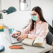 Ihre Pflichten als Arbeitgeber Junge Frau sitzt mit Maske am Schreibtisch im Homeoffice.