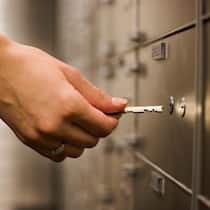 Zu welchem Banksafe gehört der Schlüssel? Eine Frau öffnet mit einem Schlüssel ein Schliessfach bei einer Bank. Hinterlässt eine verstorbene Person einen Schlüssel zu einem Banksafe, können Angehörige mit diesen Tipps den Aufenthaltsort herausfinden.