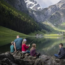 Wander-Asuflüge mit Kindern – diese Tipps sorgen für gute Laune Familie sitzt am See - Damit die Kinder keine schlechte Laune beim Wandern bekommen, sollte man ein paar Punkte beachten